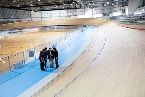 Professor and small group of students huddle on velodrome cycling track.