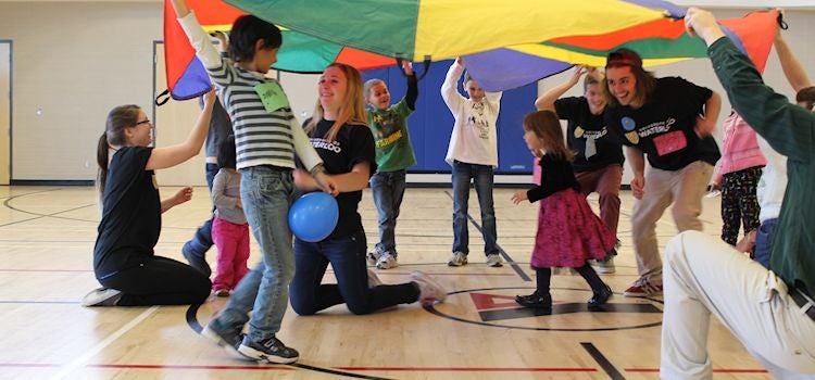 Student volunteers play parachute game with group of kids.