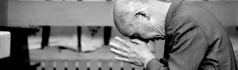 man bent over in prayer with hands to forehead