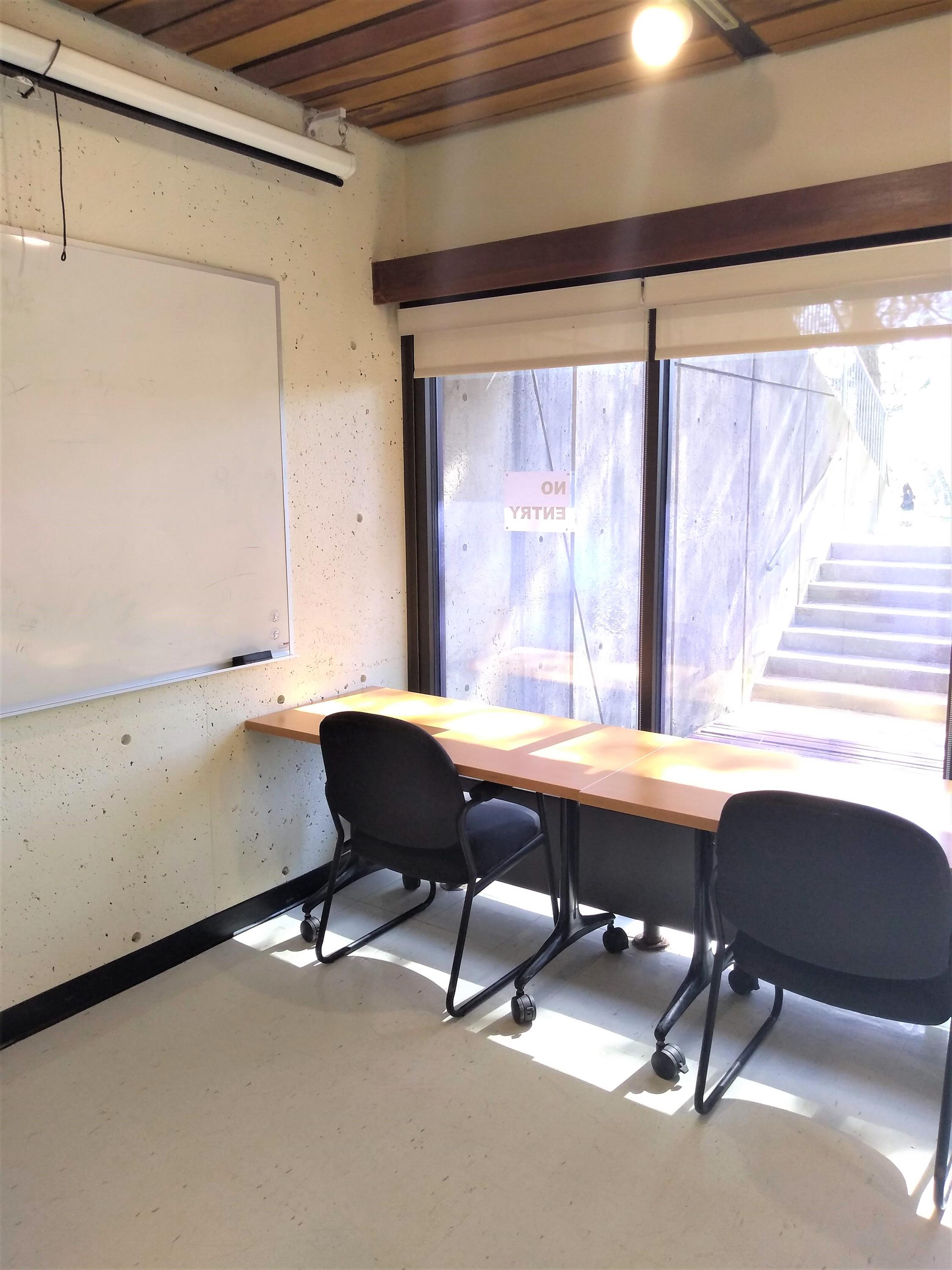 The left side of the room has a whiteboard, a projector and projector screen, and an exit door leading to an outdoor patio.