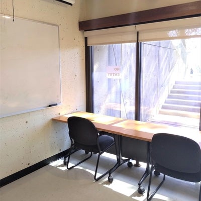 The left side of the room has a whiteboard, a projector and projector screen, and an exit door leading to an outdoor patio.