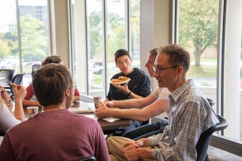 Students and faculty chatting and eating pizza.