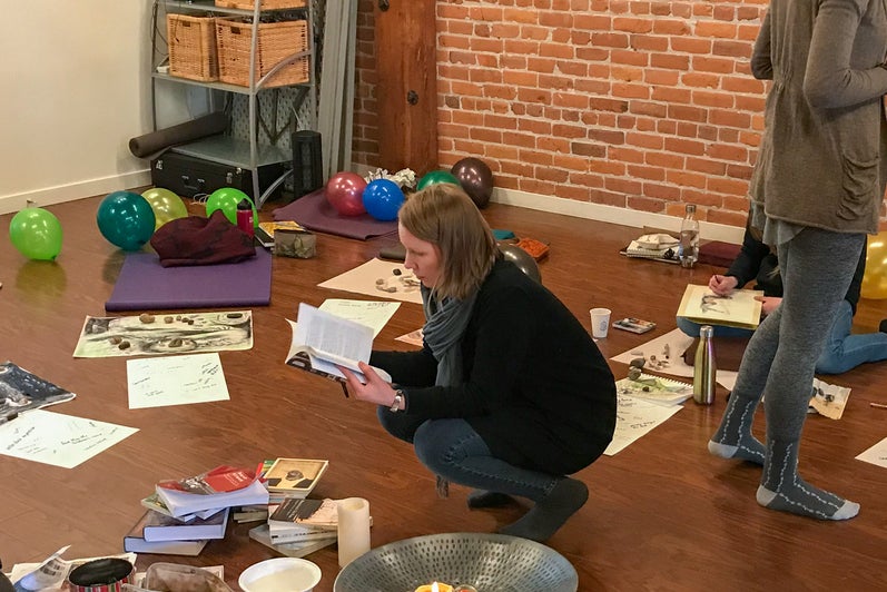 People sitting on the floor with art supplies, papers, books, candles, and balloons in a workshop space.