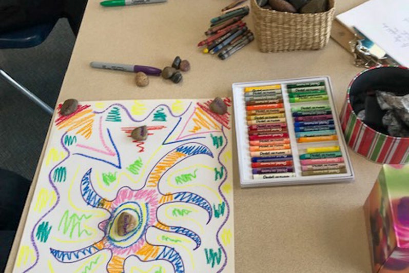 Art supplies, stones, and colourful drawings spread across a table during a creative activity.