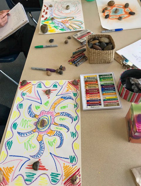Art supplies, stones, and colourful drawings spread across a table during a creative activity.