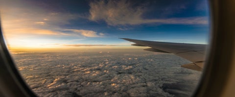 view from an aiplane window of clouds, sunset and an airplane wing