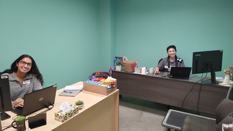 Two people looking up from desks and smiling at the camera. 