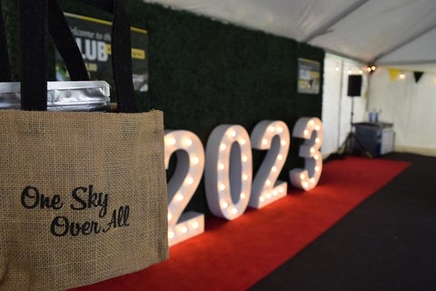 2023 Convocation sign, with marquee in background and Renison bag with one sky over all in the foreground.