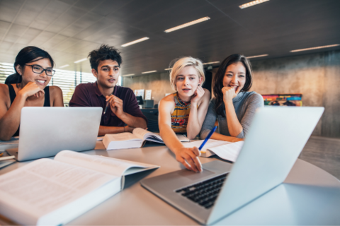 Four students sitting at a desk in front of two laptops. 