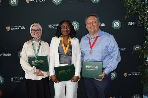 Three people standing in front of a Renison backdrop. They are each wearing a medal and holding a folder with the Renison logo on it.