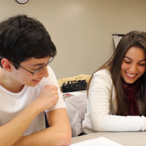 Two students talking and looking at a paper on a desk. 