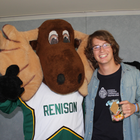 Student standing beside Renison mascot, Reni Moose. 
