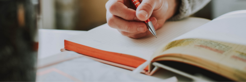 A person's hand is shown writing in a notebook. 