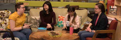 Four students sitting in a semi-circle on a couch and chairs, talking. 