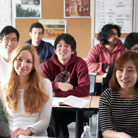 Students sitting in a classroom at desks, facing the front of the room. 