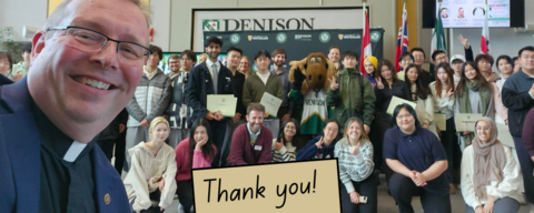 Dr. Marc Jerry taking a selfie with a group of students. There is a sign in front with "Thank you" written on it. 