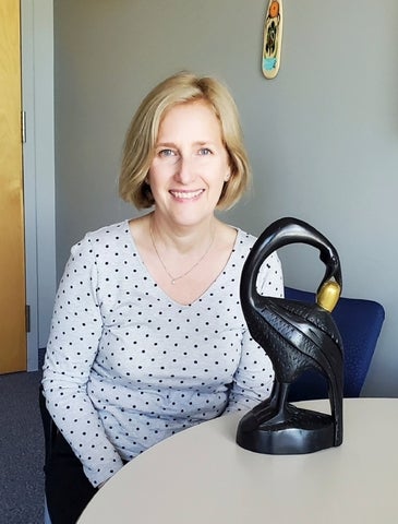 Board Chair Karen Spencer sitting beside a sculpture of a bird with its neck curved. The bird is holding a golden egg in its mouth. 