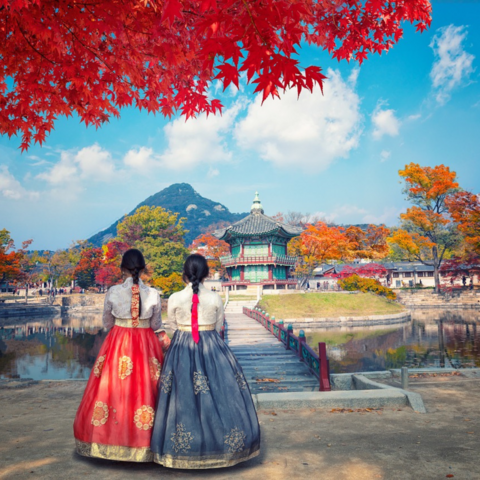 Korean women wearing traditional garments, with a temple in the background. 