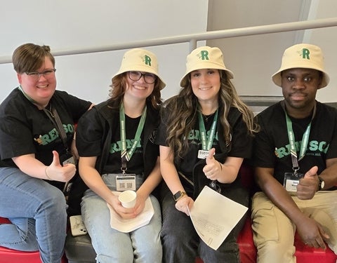 4 students in bucket hats sitting together, smiling at the camera. 