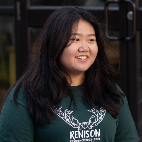 Student smiling and looking to the right of the frame. They are wearing a tshirt with Renison on it and a moose. 
