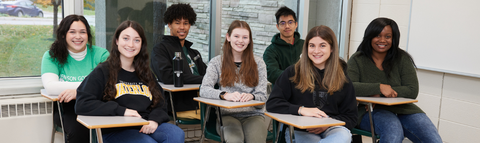7 students sitting at desks smiling at camera