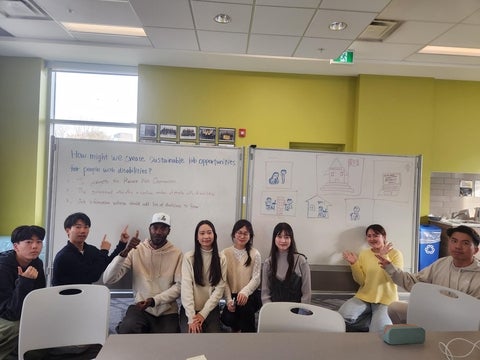 A group of students sit in front of whiteboards. The whiteboards have the question: how do we create sustainable job opportunities?