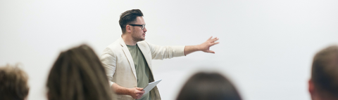 a classroom with a men standing at the front pointing at the white board