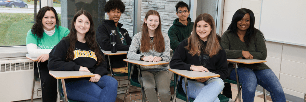 six students sitting in a classroom at desks. 