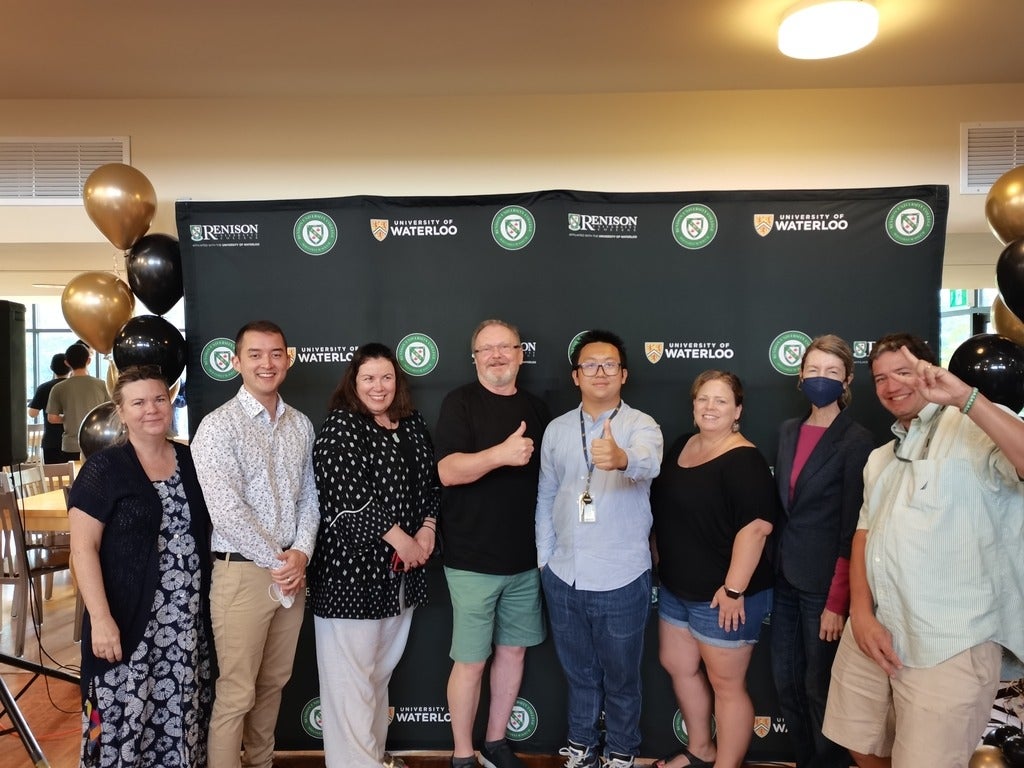 8 people standing in front of a Renison backdrop. They are smiling for the camera. 