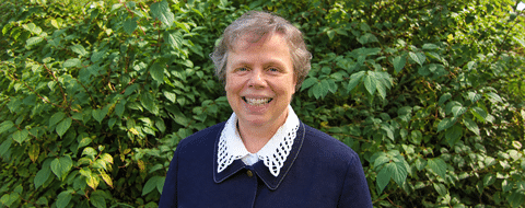 Dr. Barbara Schumacher smiling in front of a background of leaves