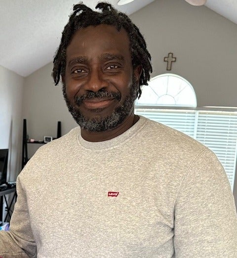 Joseph Olubobokun wearing a grey sweatshirt and smiling at the camera. 