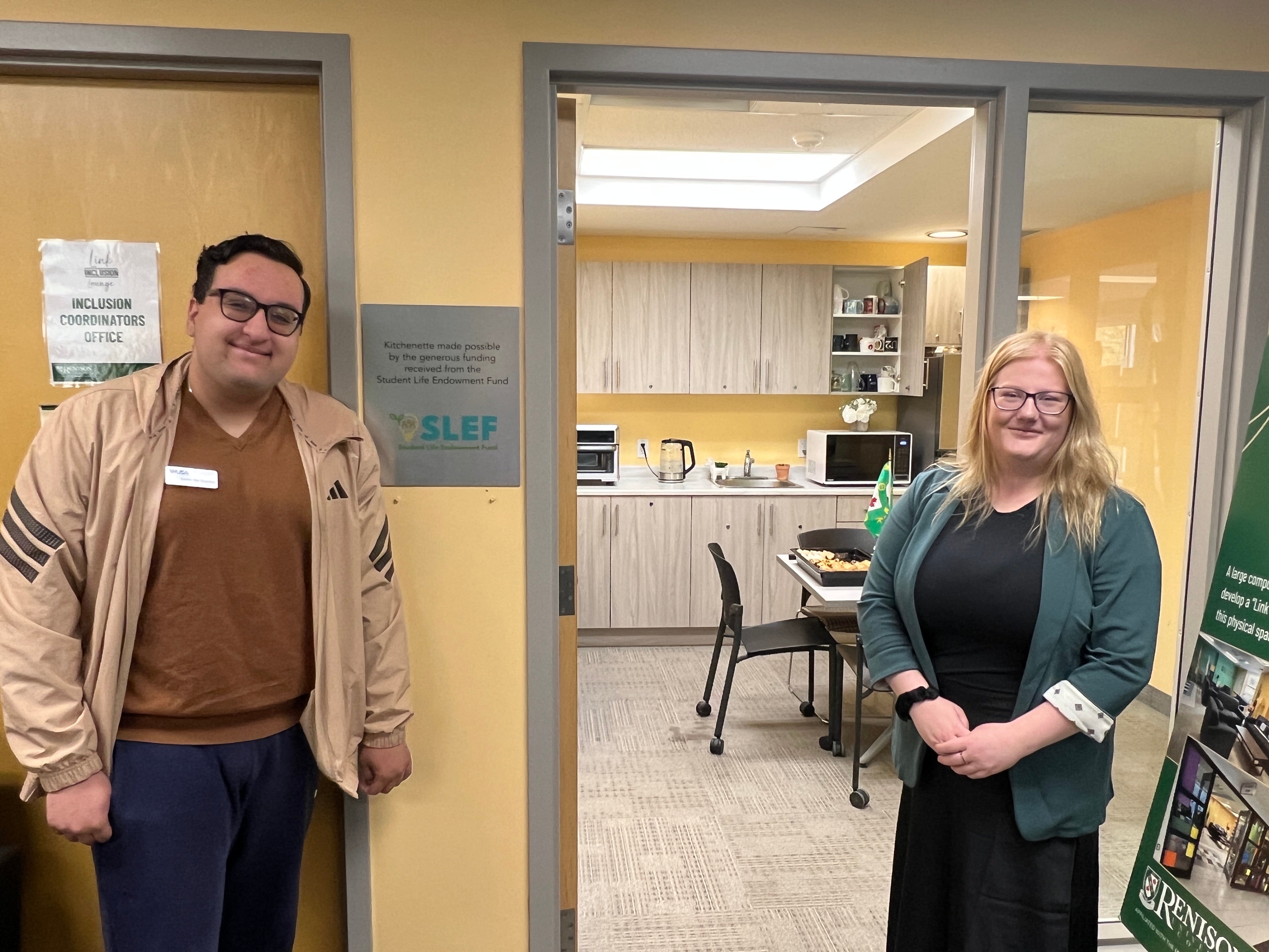 Two people standing outside of a kitchenette area