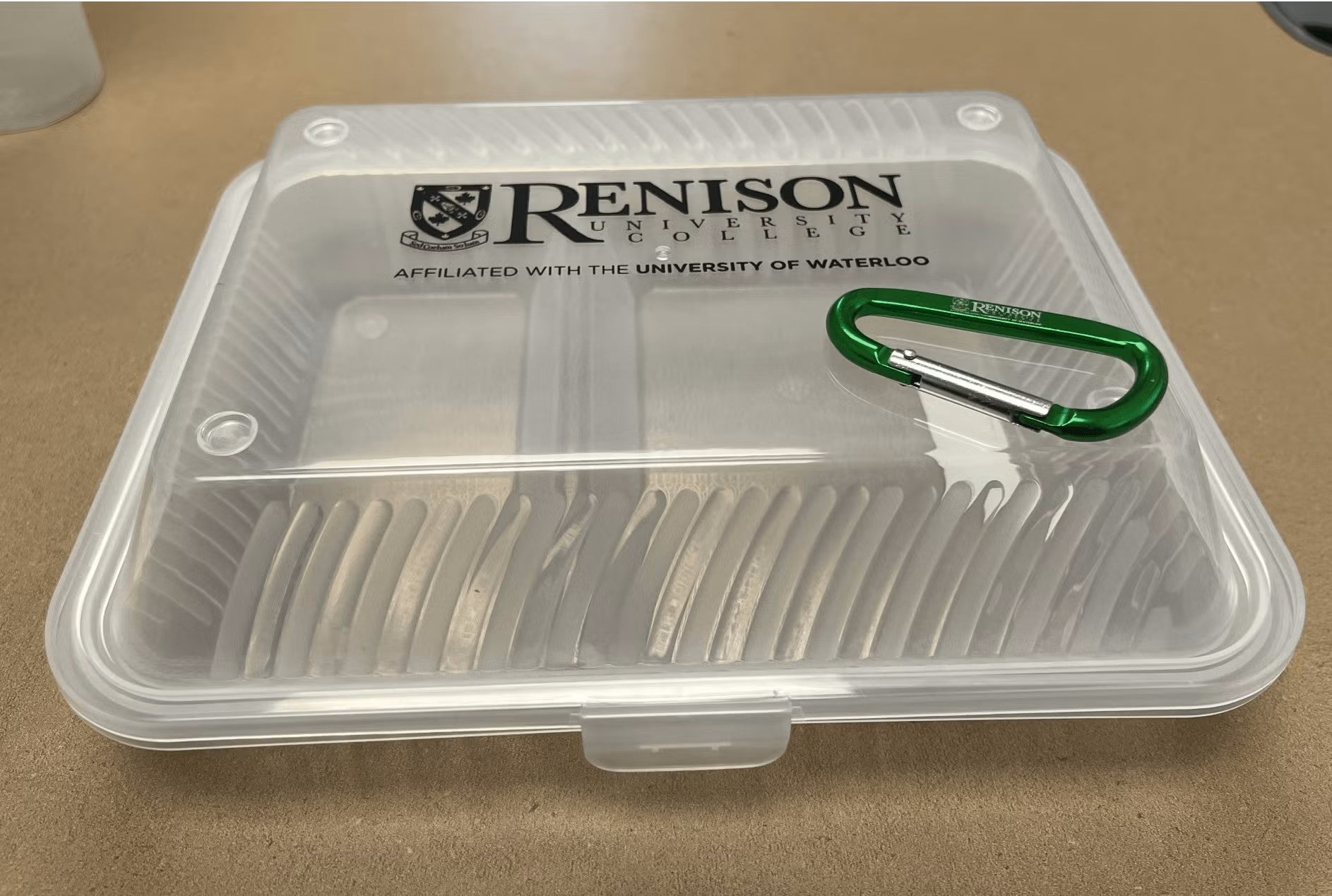 A plastic container with the Renison logo on it, and set on top of it is a green carabiner. 