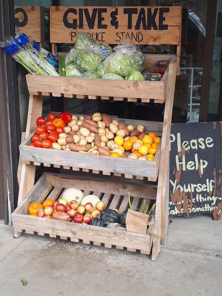 Fruit and vegetable stand with a sign saying 'give and take.' The 
