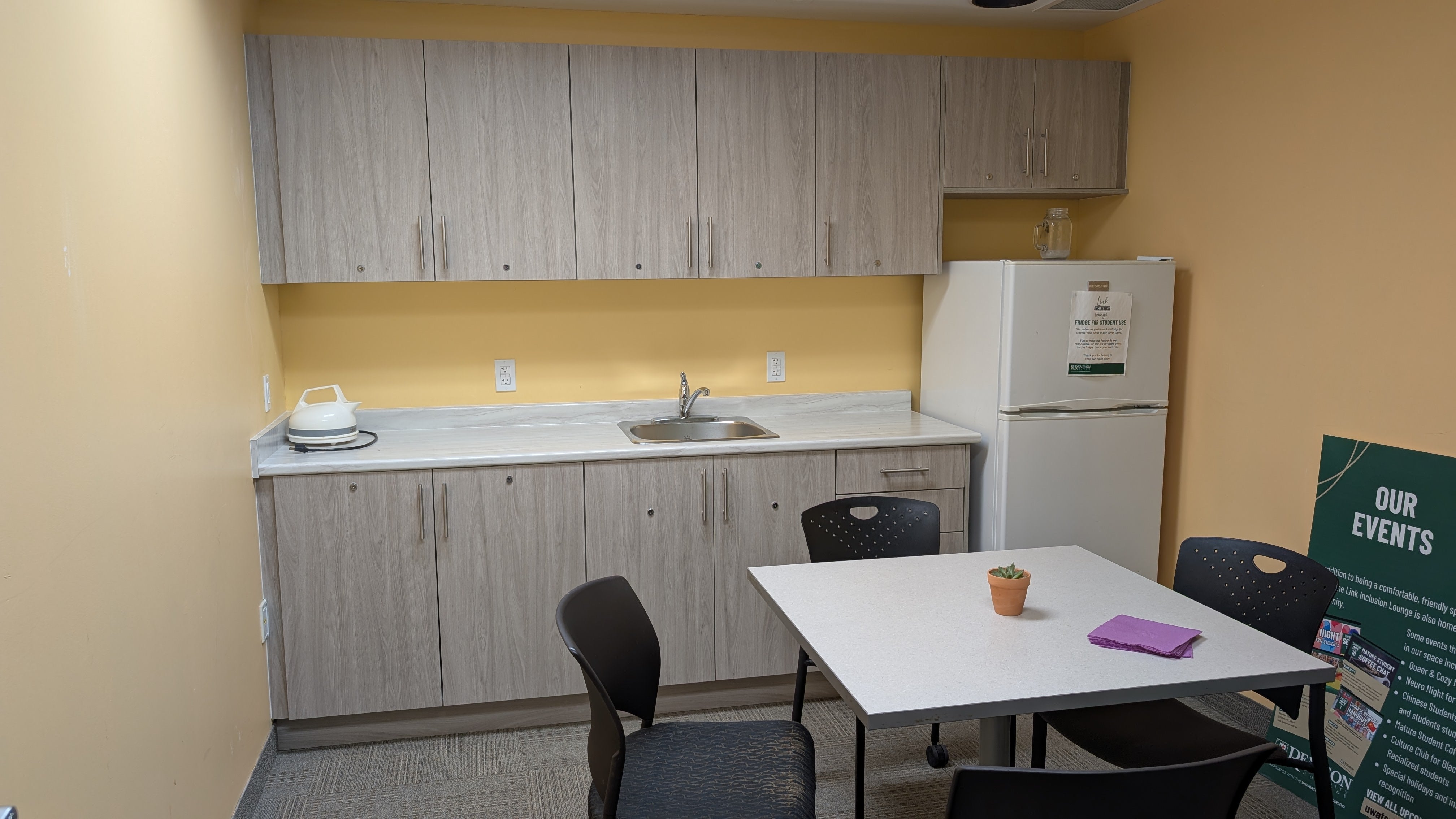 A basic kitchen with a counter, fridge, and a table with chairs. 