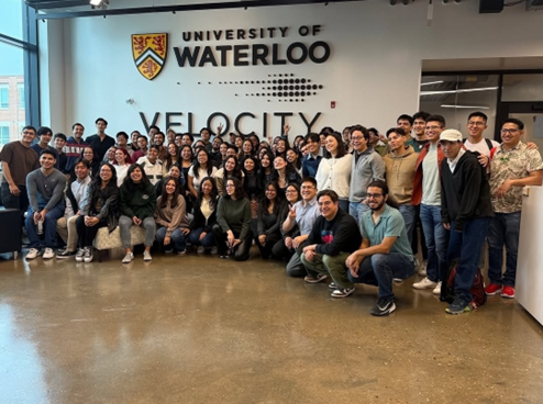 A large group of students standing in front of the University of Waterloo Velocity sign. 