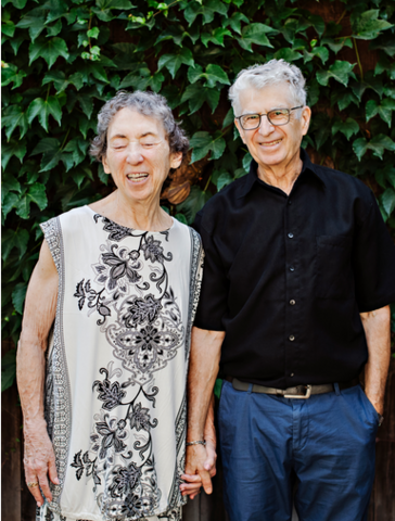 An old man and woman smiling and holding hands