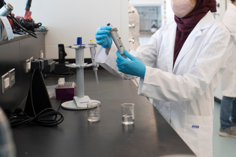 Female researcher standing in front of a lab bench holding lab equipment