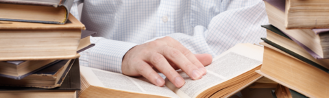 Person reading a book with additional books piled high on either side