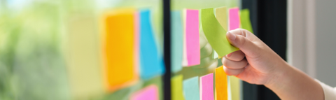 Person holding a sticky note in front of a window with several other sticky notes attached