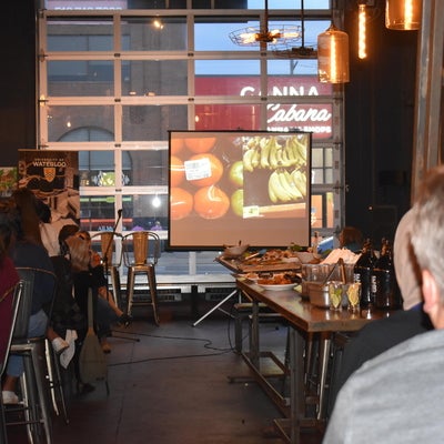 A projector screen with an image and people sitting at tables indoors.