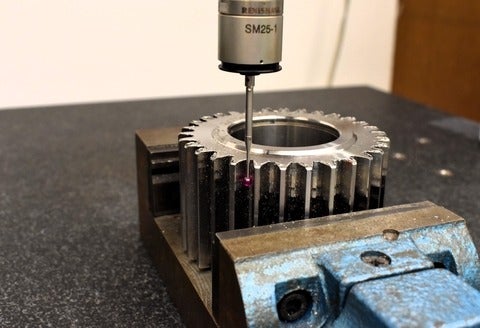 A metal gear in a clamp and a machine cutting tool on a work bench