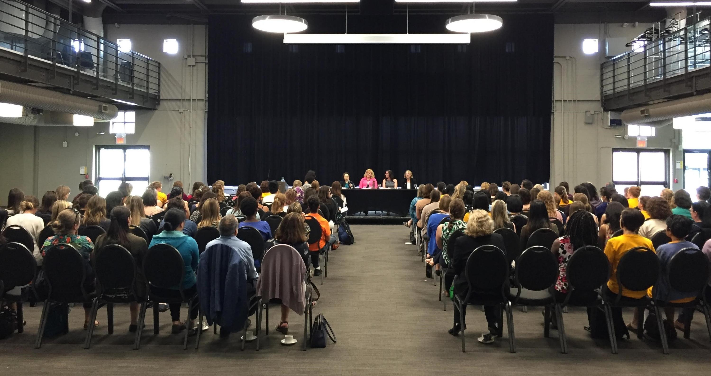 Four women speaking on a panel to a large audience