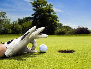 A gloved hand of a golfer flicking a golf ball into the hole.