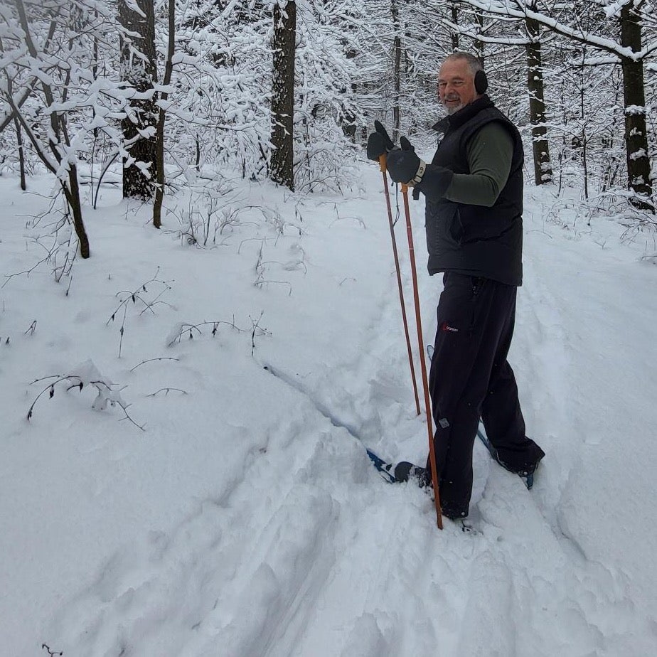 A person in a snowy woodlot trail on skis.