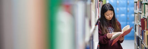 A student flips through a book in the library stacks