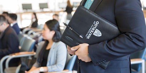 Student standing in the Tathem Centre holding a UWaterloo padfolio