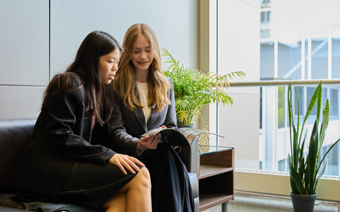 Students in professional attire sit on a couch to examine a book together