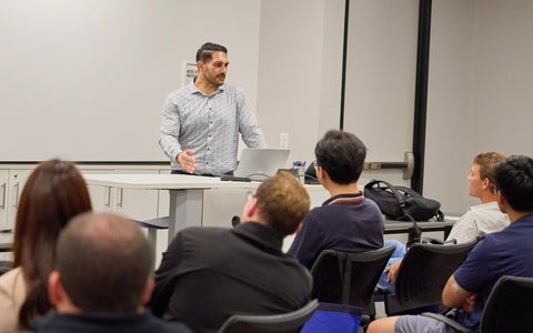Sam Al Sabery stands at the front of a classroom to address a group of university students.