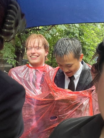 Students share a rain poncho in their suits